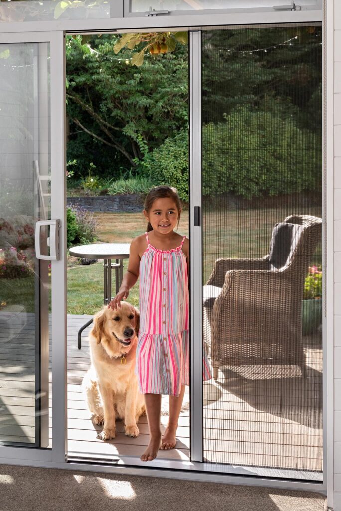 Girl and her pet dog opening her retractable fly screens katikati